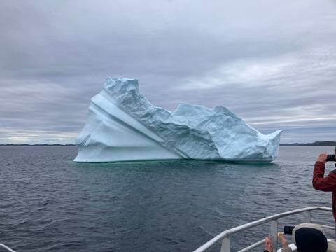 An iceberg in the ocean with a person taking a photo from a boat.