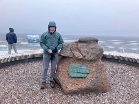 A person standing next to a rock with a plaque by the ocean.