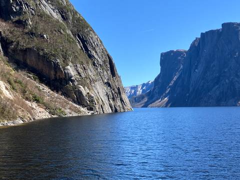 A scenic view of a fjord or lake with steep cliffs under a clear blue sky.