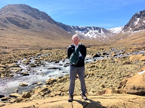Person standing in a rocky valley with a small river and clear sky.