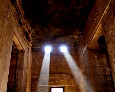 Interior of an ancient temple with beams of light streaming through small windows.