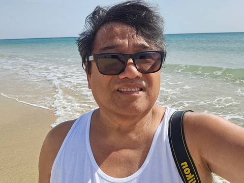 A person taking a selfie at the beach with the sea in the background.