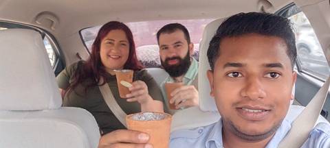 Group of people inside a car, holding clay cups and smiling.