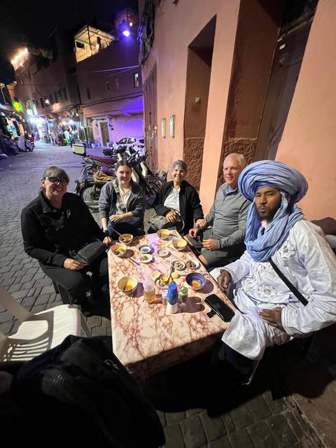 Tourists sitting at an outdoor restaurant table with traditional dishes.