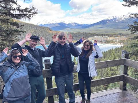 Four people making funny poses with a vast landscape and a large lodge in the background.