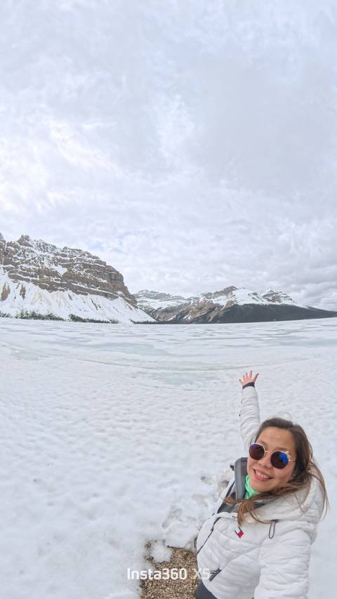 Snow-covered mountains with frozen lake and hand in view.