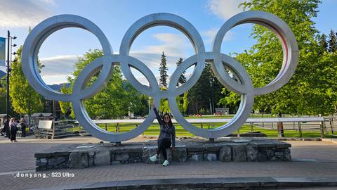 Person sitting in front of Olympic rings monument.