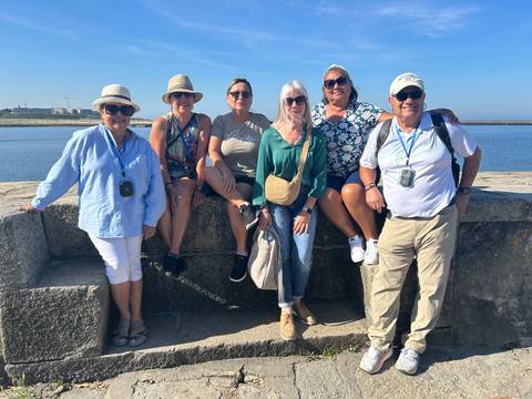Group of tourists sitting on a stone ledge by the water.