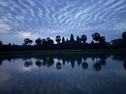 Silhouette of ancient temple reflected in water during dawn.