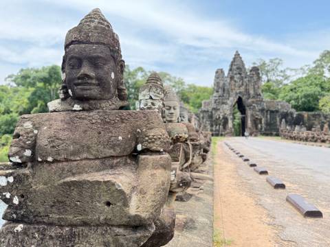 Rows of stone statues lining a bridge leading to an ancient building.