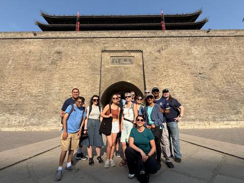Group of tourists posing in front of an ancient stone wall under bright sunlight.