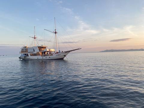 Sailing boat on calm waters at sunset with an island in the distance.