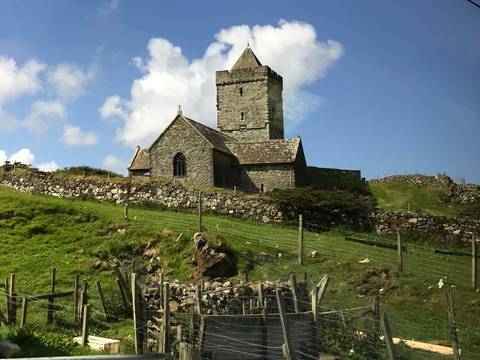 Stone church on a grassy hill under a blue sky.