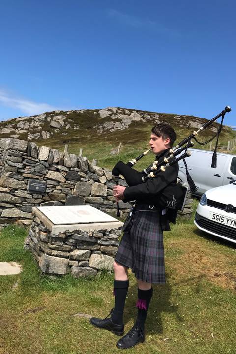 Bagpiper in traditional clothing playing in a natural setting.