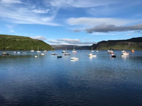 Harbor with boats anchored on a calm, reflective water surface surrounded by hills.