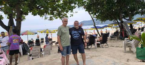 Two people posing on a beach with chairs and umbrellas.