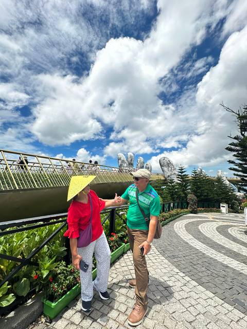 A couple standing on a walkway with large hand structures in the background.
