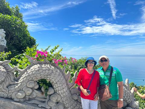 Couple posing by a detailed sculpture with an ocean view.