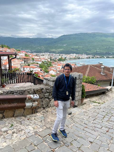 A person posing with a view of a town and lake in the background.