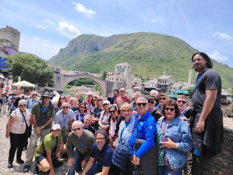 Group photo of tourists with a historic bridge and landscape.