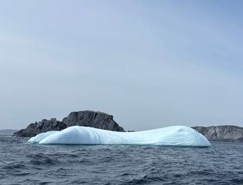 Iceberg floating near rocky islands in overcast weather.
