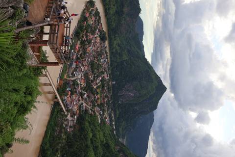 Elevated view of a town with a river and bridge, set against lush hills.
