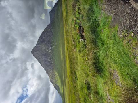 Mountain landscape with green fields and a cloudy sky.