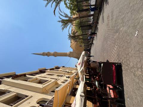 Street with a tall minaret and outdoor seating.