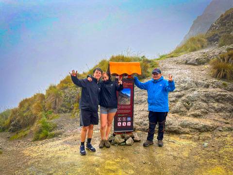 Three hikers posing at a sign on a foggy mountain trail.