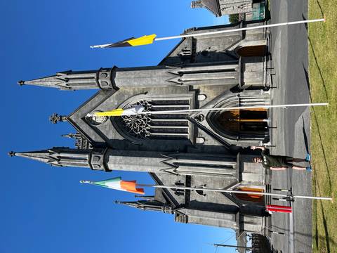 A person standing in front of a large stone cathedral with flags.