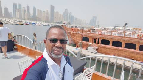 Person taking a selfie on a boat with a cityscape in the background.