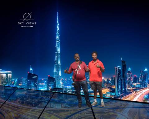 Two people posing in front of a skyscraper at night.