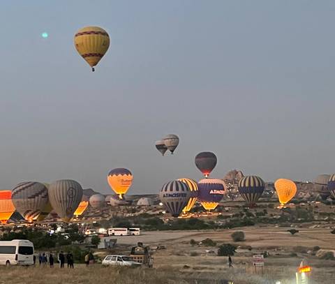 Hot air balloons rising over a valley at dusk.