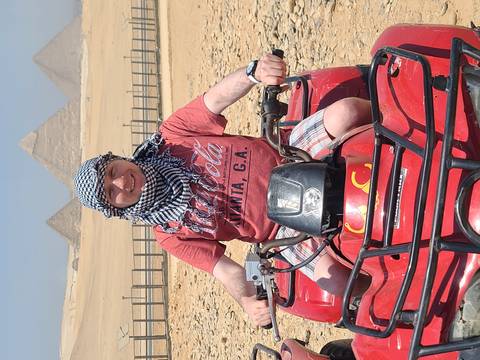 Person riding an ATV in the desert with pyramids in the background.