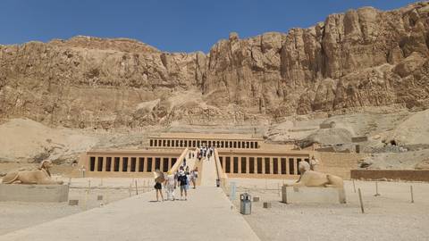 A temple with large statues and tourists on steps.