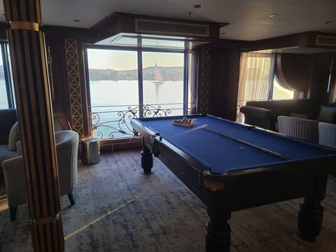 Interior of a ship with a pool table and view of a river.