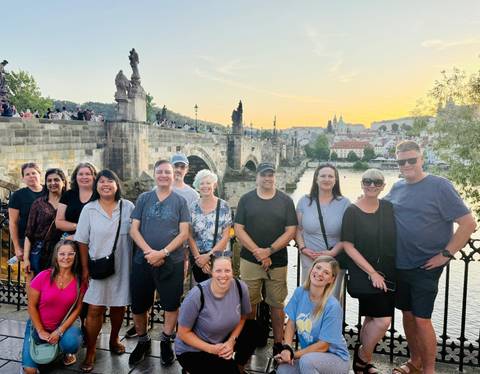 Group of tourists posing in front of a historic bridge at sunset.
