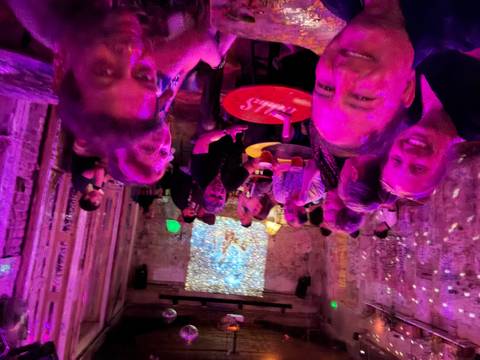 Group of people sitting in a dimly lit bar with colorful lighting.