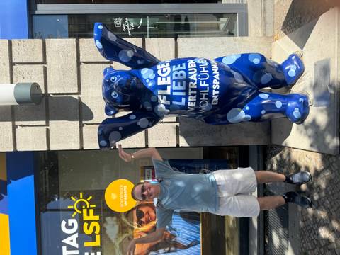 Man posing with a painted bear statue in an urban area.