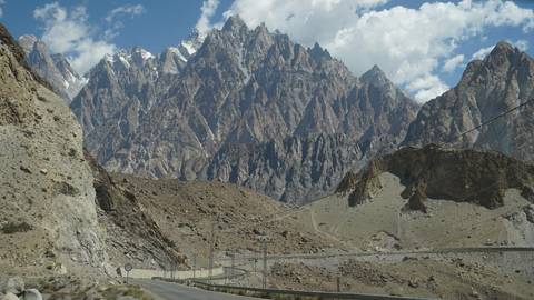 Road through rugged terrain with high rocky peaks.