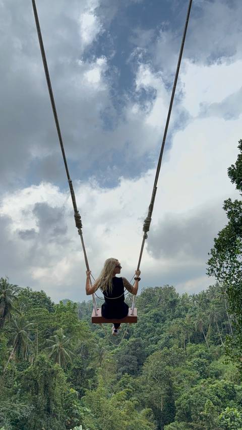 Individual on a swing with a cloudy sky backdrop.