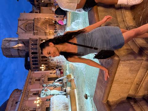 Woman at a fountain in a vibrant night setting, smiling.
