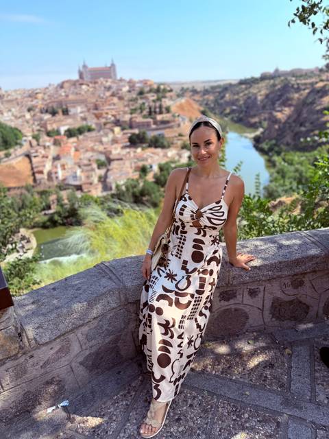 Woman leaning on a stone fence with scenic background of a town by a river.