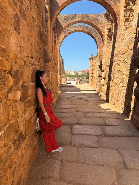Woman in red dress leaning against an ancient stone wall.