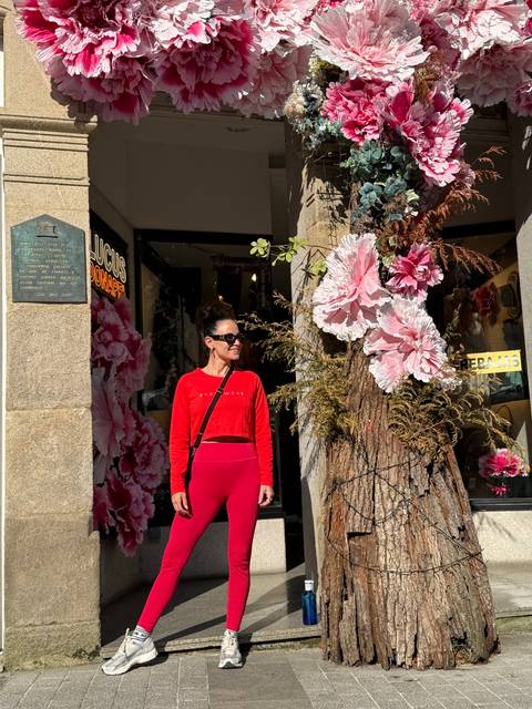 Woman posing outside a floral shop decorated with large pink flowers.