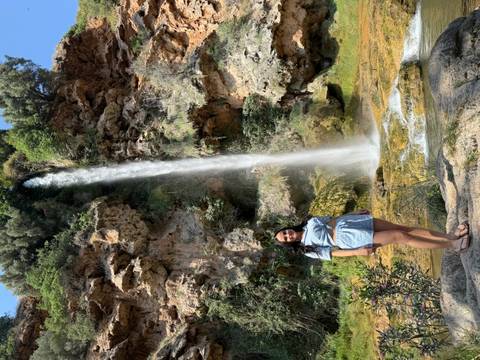 Woman standing in front of a tall waterfall.
