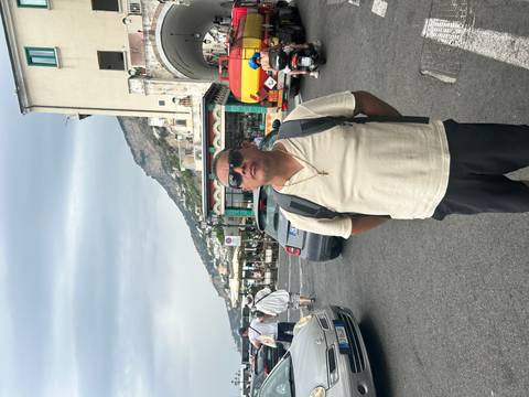 Person standing on a street with traffic and a scenic mountain and coastline in the background.