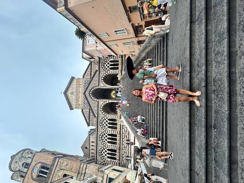 Person posing on steps in front of a cathedral with people in the background.