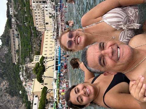 Three people smiling in a crowded beach setting with buildings in the background.