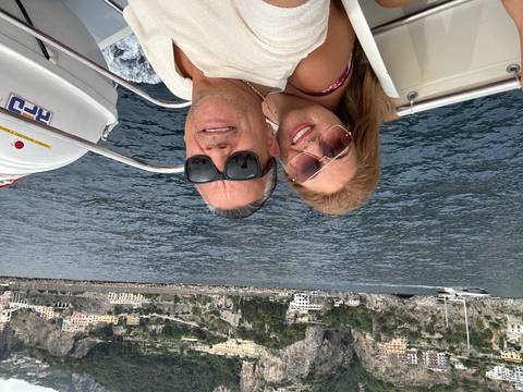 Two people on a boat with Positano coastline in the background.